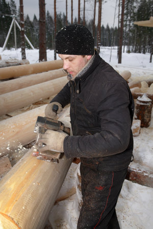 Leningrad Region, Russia - February 2, 2010: Processing logs for building log, removing the bark using a planing machine.のeditorial素材