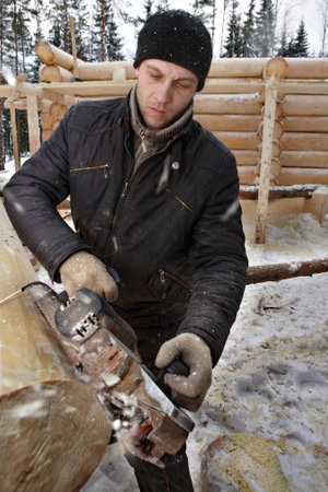 Leningrad Region, Russia - February 2, 2010: Young man planes the logs for log construction.のeditorial素材