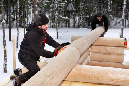 Leningrad Region, Russia - February 2, 2010: Log Home Construction Handcrafting, two workers doing assembly of the wall made of logs.のeditorial素材