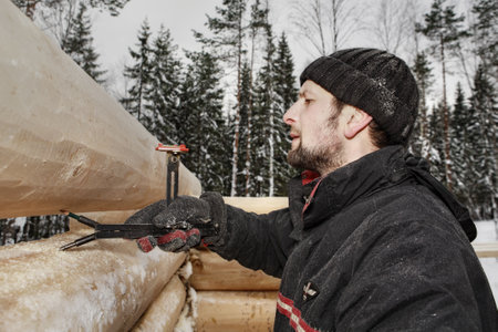 Leningrad Region, Russia - February 2, 2010: Woodworker makes marks on a log surface, using scriber tool equipped with two levels, it transforms the contours of the lower log to the upper one.のeditorial素材