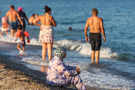 Antalya, Turkey - 25 august, 2014: A Muslim woman sits on the beach dressed in Muslim clothing, a hijab and a shirt with a long sleeve and a long hem.のeditorial素材