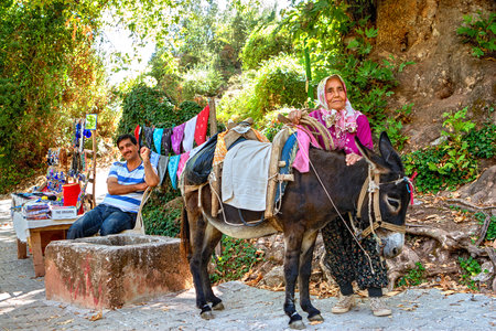 Antalya, Turkey - 26 august, 2014: An old Turkish woman and a saddled donkey are standing next to a roadside trader on a mountain road.のeditorial素材
