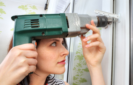 The girl makes fixing holes under the window limiter, using an electric drill.の写真素材