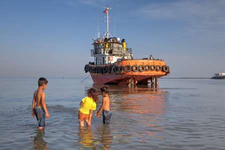 Bandar Abbas, Hormozgan Province, Iran - 16 april, 2017: Three young children, about 7 years old, two little girls, and one boy playing in the water of the Persian Gulf, near the jammed boat.のeditorial素材