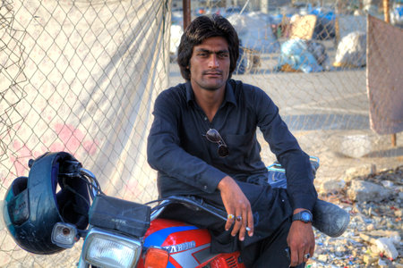 Bandar Abbas, Hormozgan Province, Iran - 16 april, 2017: A portrait of an Afghan man who is resting in the shadows, sitting on the saddle of his motorcycle.のeditorial素材
