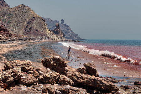 Hormuz Island, Hormozgan Province, Iran - 17  april, 2017: Iranian Island of Hormuz in Persian Gulf, A lone traveler walks on the red beach along the surf line.のeditorial素材