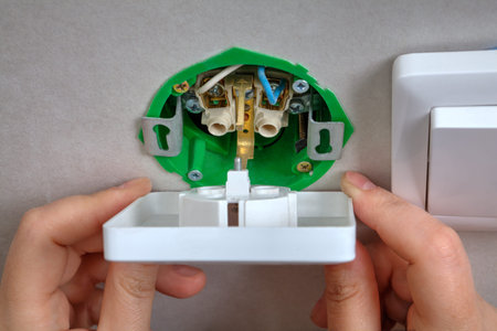 Installing the wall outlet into a wiring box, close-up hands of an electrician.