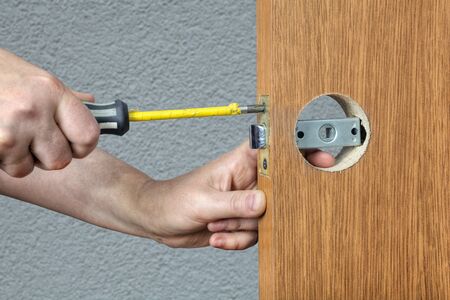 Screwdriver in the hands of a locksmith close-up, replacement of the lock in the interior door.の写真素材