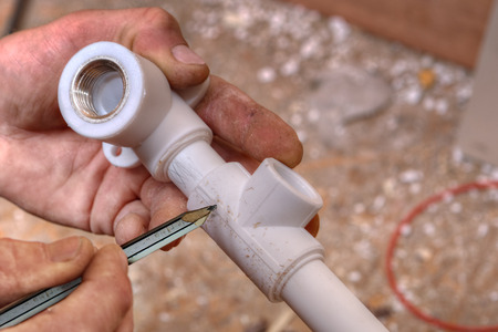 The plumber makes markings on plastic fittings using a pencil, close-up of the hand.の写真素材