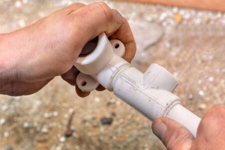 The plumber connects parts of the plastic water pipe using fittings, hands close-up.の写真素材