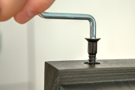 Screw the furniture screw into the wood plank using the hex key, close-up.の写真素材