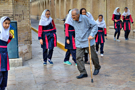 Fars Province, Shiraz, Iran - 18 april, 2017: An elderly man with a cane walks past a group of girls in school uniform.のeditorial素材