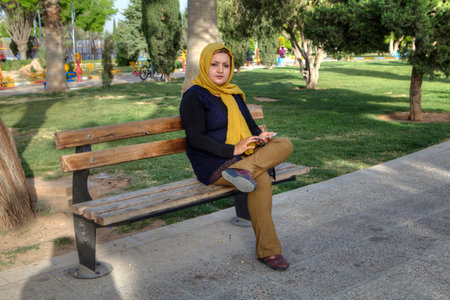 Fars Province, Shiraz, Iran - 19 april, 2017: Young Muslim woman in a yellow headscarf sitting alone on a park bench.のeditorial素材