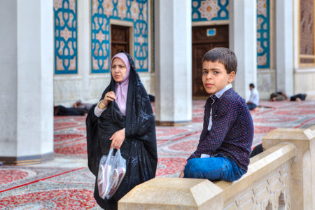 Fars Province, Shiraz, Iran - 19 april, 2017: Shah Cheragh Shrine, Muslim woman wearing an Islamic veil passes by one of the unknown boy, about 10 years old.のeditorial素材
