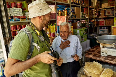 Yazd, Iran - April 22, 2017: The tourist talks with an elderly Iranian grocer in the interior of a grocery store.のeditorial素材