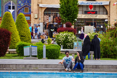 Isfahan, Iran - April 24, 2017: A young Iranian couple is sitting near a mosque in front of a fountain on a date and gaily chatting, the Naqsh-e Jahan Square.のeditorial素材