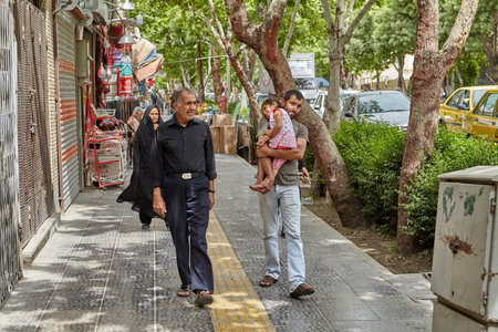 Isfahan, Iran - April 24, 2017: an Iranian man walks down the street and carries his daughter in his arms, there are people walking nearby.のeditorial素材