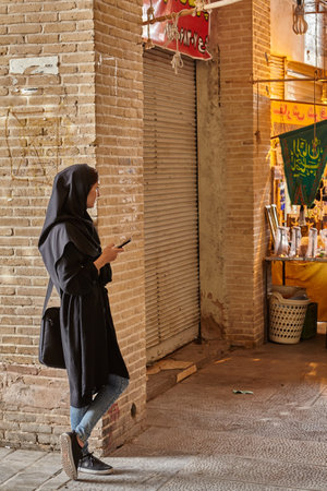 Isfahan, Iran - April 24, 2017: Iranian girl in hijab stands near wall in market with mobile phone in hand.のeditorial素材