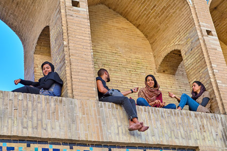 Isfahan, Iran - April 24, 2017: A young man talks to the girls, sitting on an arched niche of a stone bridge.のeditorial素材