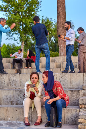 Isfahan, Iran - April 24, 2017: Two modern Iranian girls, dressed in a mandatory hijab, view the images on the screen of a mobile device.のeditorial素材
