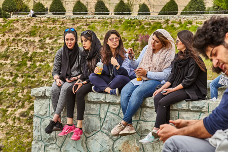 Tehran, Iran - April 28, 2017: Iranian students in hijabs are sitting in the park, chatting with...