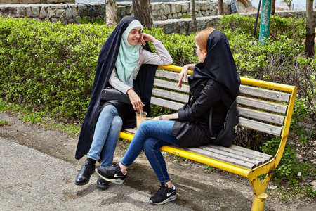 Tehran, Iran - April 28, 2017: two Iranian women in hijabs sit on a bench in the park and talk.のeditorial素材