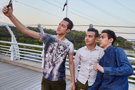 Tehran, Iran - April 28, 2017: Three Iranian young men make selfies on Tabiat Bridge, using a mobile...