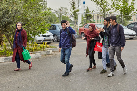 Tehran, Iran - April 29, 2017: Three young men and two girls in hijabs walking along the sidewalk.のeditorial素材