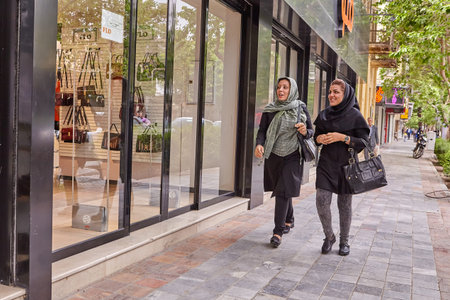 Kashan, Iran - April 25, 2017: two Iranian women in hijabs are walking along the street near a store with bags and smiling.のeditorial素材