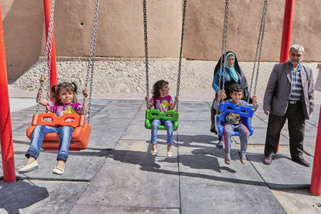 Kashan, Iran - April 26, 2017: Iranian children swing on a swing, their parents are behind them.のeditorial素材