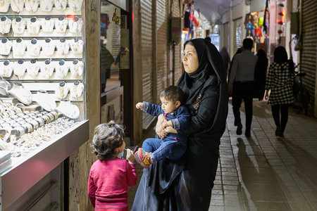 Kashan, Iran - April 25, 2017: Iranian family - a woman with a little boy in her arms and girl are standing near a jewelry store in the market.のeditorial素材