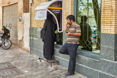 Kashan, Iran - April 27, 2017: A woman in Islamic clothes uses a street ATM, a man is waiting nearby.のeditorial素材