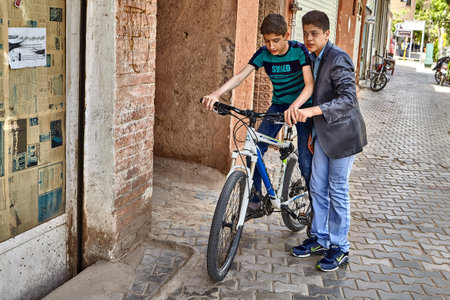 Kashan, Iran - April 27, 2017: A young man is teaching a friend to ride a bike on a city street.のeditorial素材
