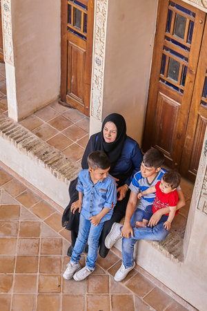 Kashan, Iran - April 26, 2017: Iranian woman in hijab sits on the steps in front of the door with three sons in Tabatabaei historical house.のeditorial素材