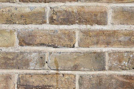 Close-up fragment of brick wall with an old, cracked brick of yellow and light brown color, seams...