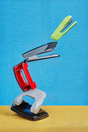 Few colored hole punchers and staplers float in air under non gravity conditions on a blue backdrop.の写真素材