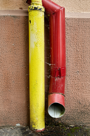 Red gutter pipe downspout for rain water and yellow tube for gas pipeline fixed on facade of residential building.の写真素材