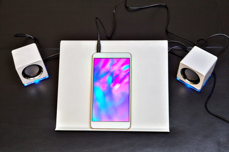 The smartphone is placed in a plastic holder and connected to white mini speakers with blue led...