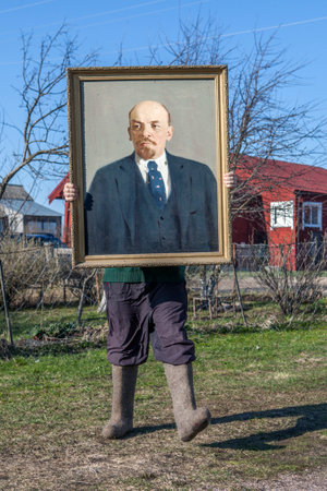 Karelia, Russia - May 1, 2016: Russian village in the spring time, day, peasant, shod in felt boots, holding an oil portrait of Vladimir Lenin, the leader of the Communists of the Soviet Union.のeditorial素材