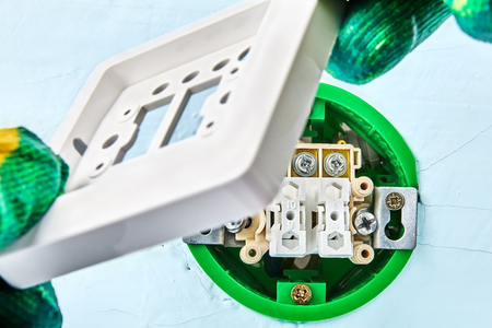 Electrician is putting  part of european  light switch on round outlet box for wall light, electrical work.の写真素材