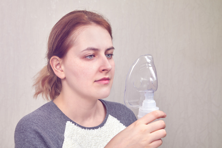 Young woman is going to use nebulizer mask to breathe through it, because she has respiratory diseases.の写真素材