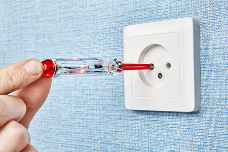 Electrician is inserting tester screwdriver with one contact and red LED lamp into a hole of an...