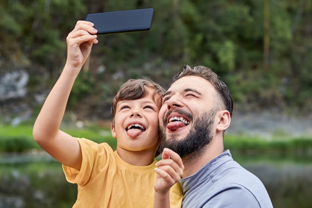 Little boy about 8 years old and his father are making faces while take pictires on the mobile phone...