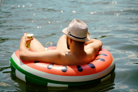 Young caucasian man with hat on his head is drifting on the inflatable ring while relaxing on the...