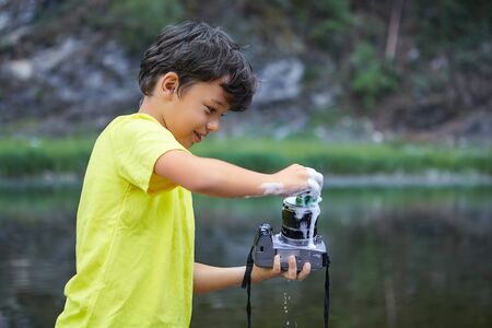 Smiling white bully boy is holding digital camera in his hands and washing it by foam in the countryside.の写真素材