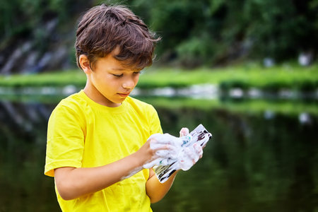 Removing dirt from the screen of a mobile phone. Little boy cares for a smartphone screen using soap...