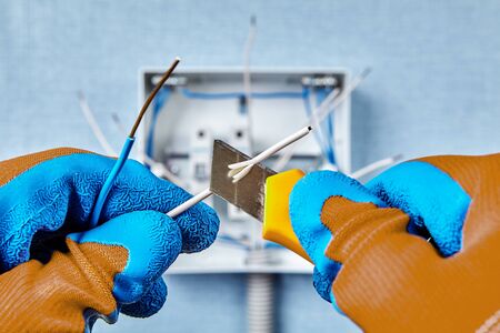 The use of a construction knife when installing a switchboard in a residential building, removing insulation from the end of a copper wire. Home electrical service, electric work.の写真素材