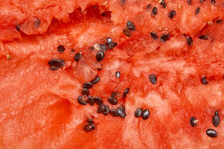 A close-up of the texture of a red fresh watermelon filling a full frame, an uneven cut with seeds and highlights, a berry was eaten with a spoon.の写真素材