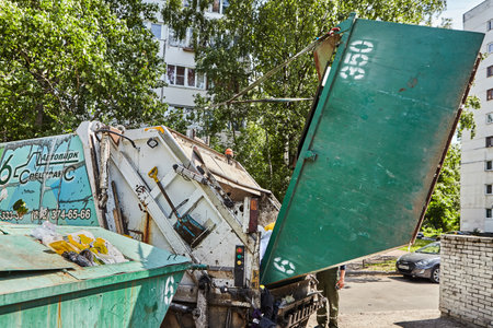 St. Petersburg, Russia - June 17, 2019: A worker empties household waste from a trash container into the body of a garbage truck.のeditorial素材