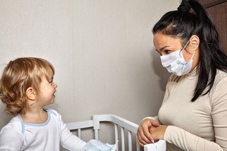 Little cute white caucasian girl about 2 years old is looking at her mather with medical mask on the face as a protection from infections during illness and   smiling.の写真素材